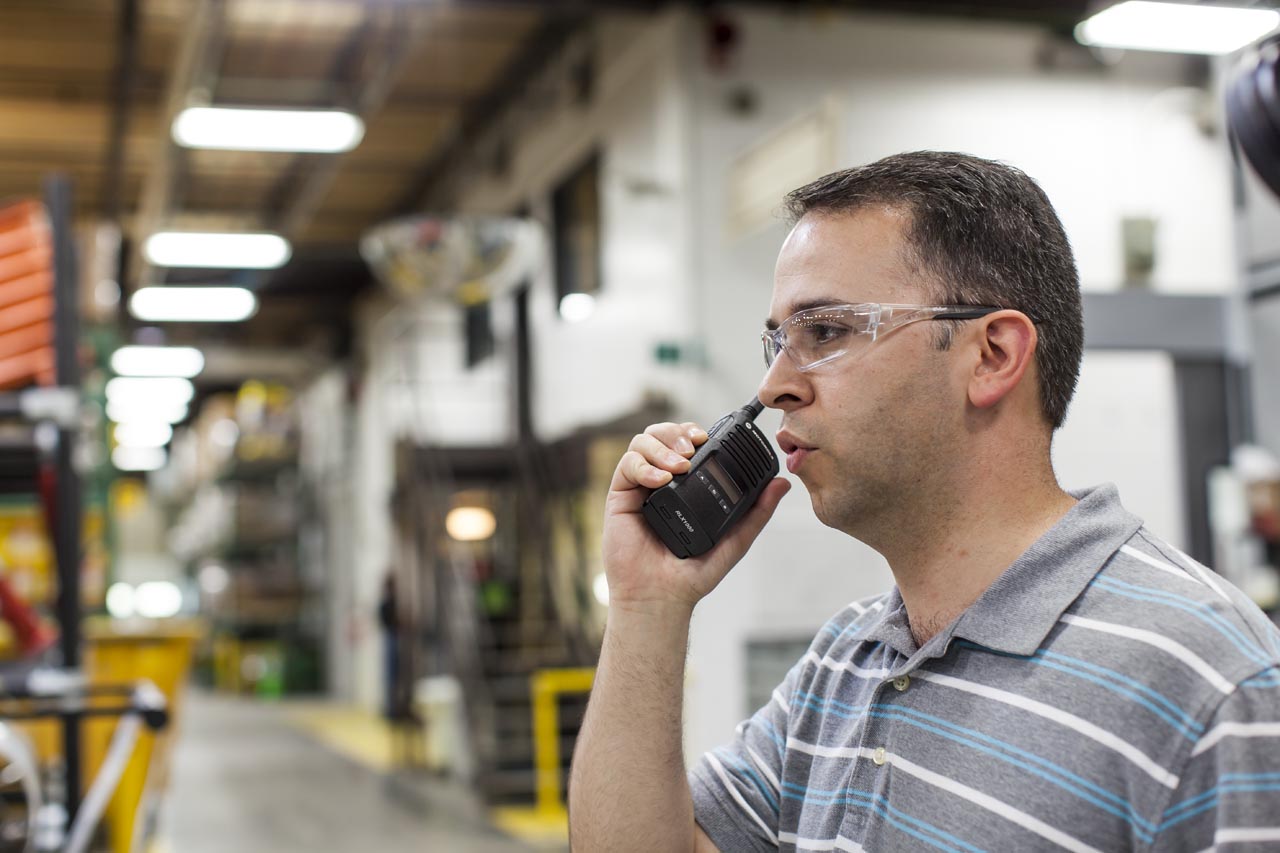 Man in warehouse holding two-way radio. Wearing protective glasses.